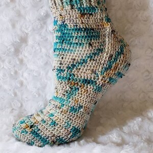 May include: A pair of crocheted socks in a blue, beige, and yellow color pattern. The socks are ankle-high and have a ribbed cuff.