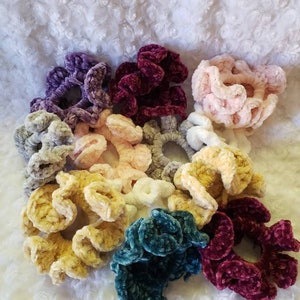 Puede incluir: Una colecci&oacute;n de scrunchies hechos a mano en varios colores, incluyendo morado, burdeos, rosa, gris, amarillo, verde azulado y blanco. Los scrunchies est&aacute;n hechos de un material suave y aterciopelado y son perfectos para agregar un toque de estilo a cualquier peinado.