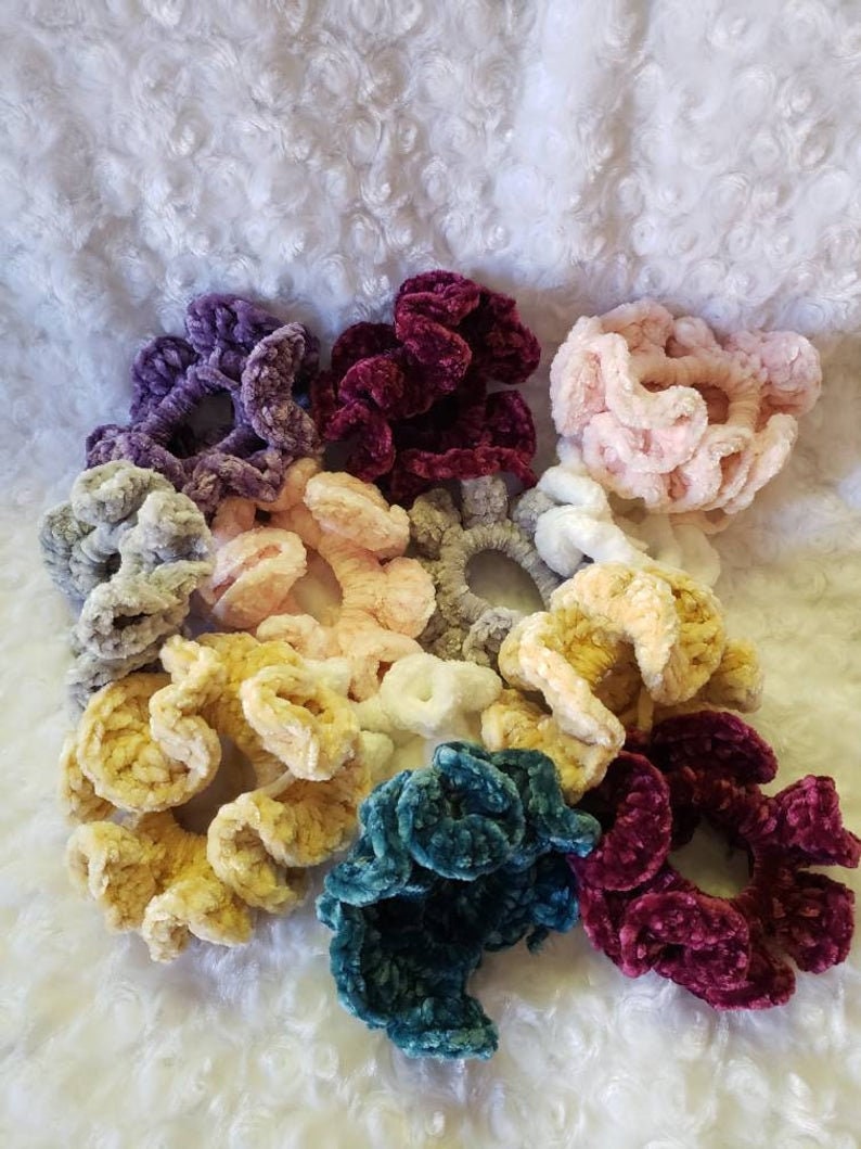 Puede incluir: Una colecci&oacute;n de scrunchies hechos a mano en varios colores, incluyendo morado, burdeos, rosa, gris, amarillo, verde azulado y blanco. Los scrunchies est&aacute;n hechos de un material suave y aterciopelado y son perfectos para agregar un toque de estilo a cualquier peinado.