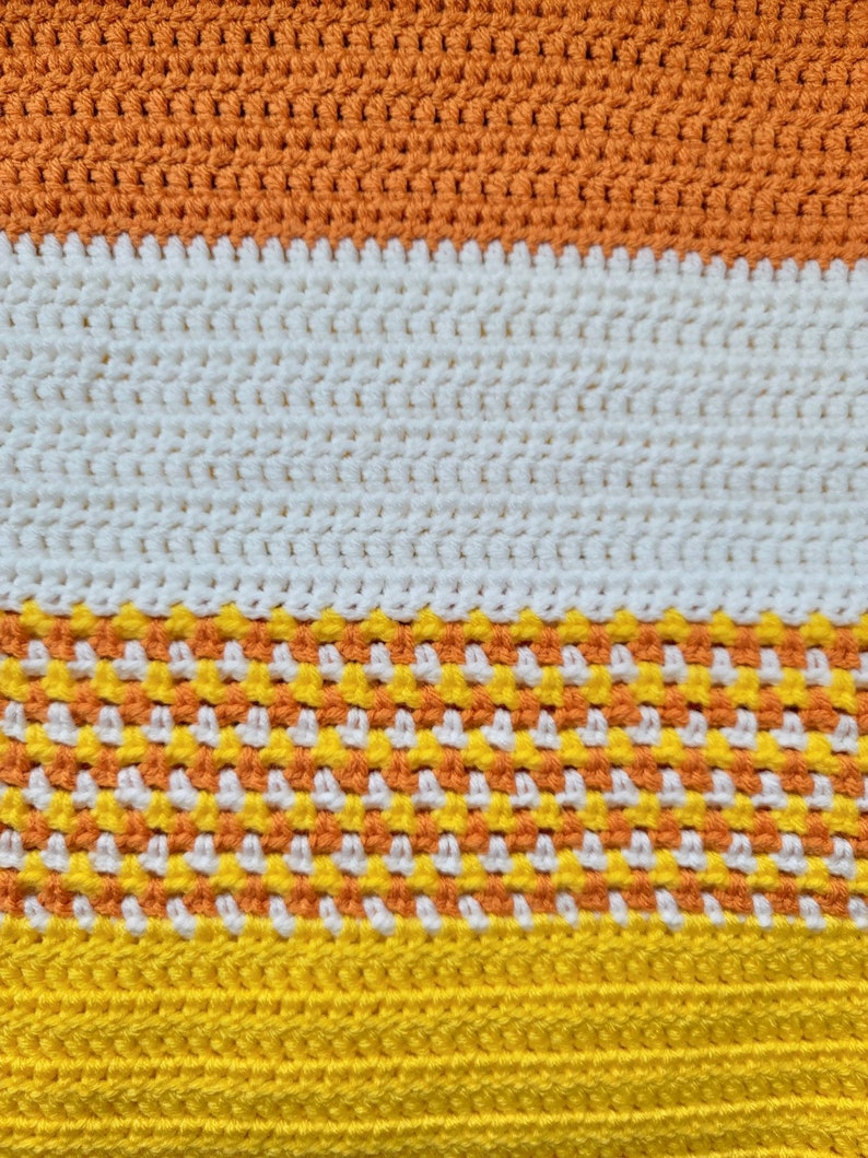 May include: A crocheted blanket with stripes of orange, white, orange and yellow yarn.