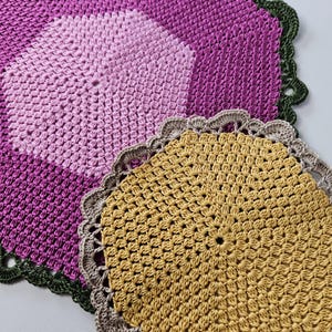 Puede incluir: Dos manteles individuales de ganchillo, uno en tonos de rosa y verde, y el otro en color amarillo dorado.