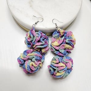 May include: A pair of crocheted earrings with a multi-colored swirl pattern in shades of pink, blue, green, and yellow. The earrings are made of yarn and have silver hooks.