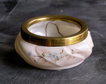 May include: A small, white, swirl-patterned porcelain trinket box with a gold metal lid and floral accents. The lid has a clear glass insert.