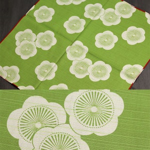 May include: Green fabric with a white floral pattern. The flowers have a circular design with a white center and green lines radiating outward.