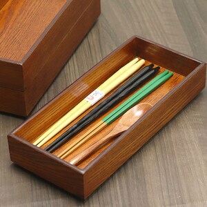 Może przedstawiać: Drewniany stojak na pałeczki z ciemnobrązowym wykończeniem. Stojak zawiera zestaw pałeczek, w tym czarne, zielone i naturalne drewniane pałeczki, oraz drewnianą łyżkę.