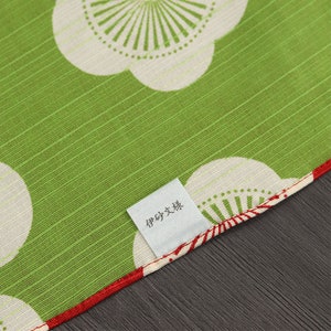 May include: A green fabric with a white and red floral pattern. The fabric has a label that says "手作り大好き".
