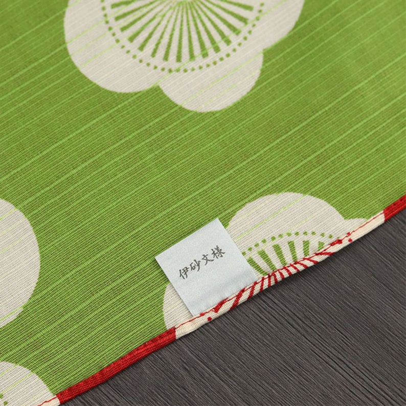 May include: A green fabric with a white and red floral pattern. The fabric has a label that says "手作り大好き".