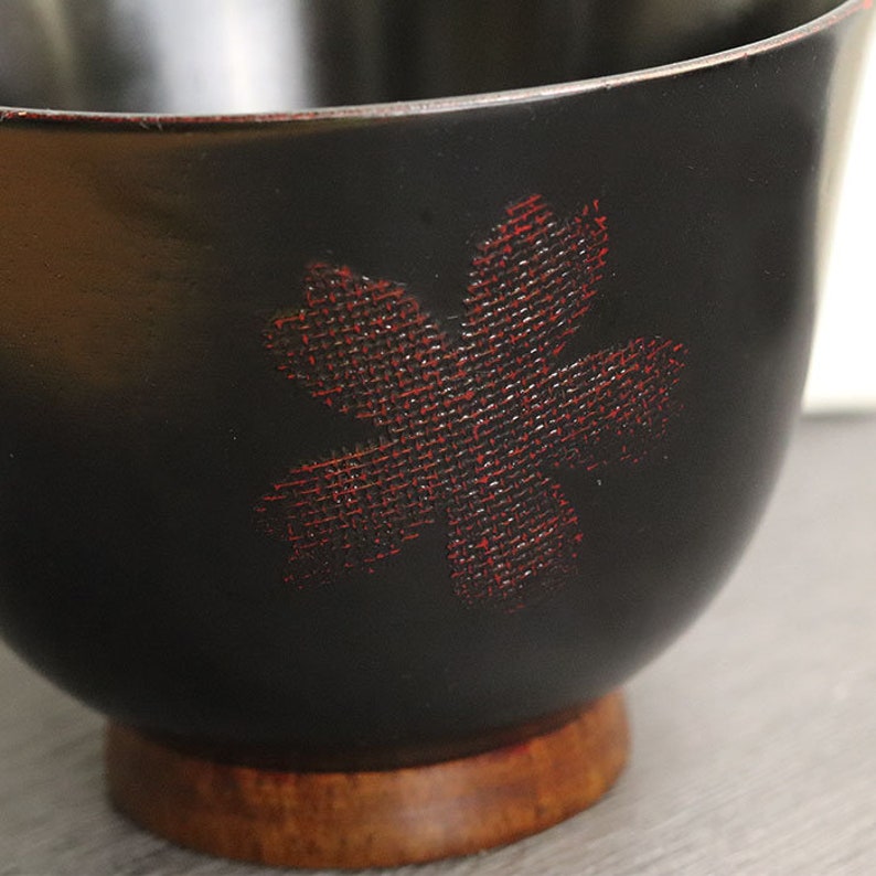 May include: A black wooden bowl with a red flower design. The bowl has a wooden base.