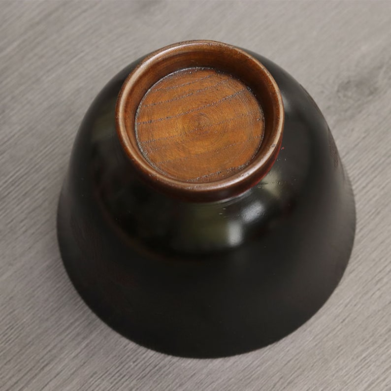 May include: Black wooden bowl with a brown wooden base. The bowl is round and has a smooth, glossy finish.
