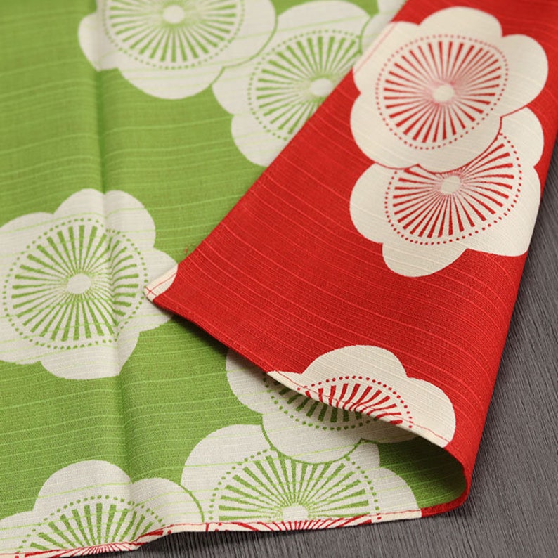 May include: Two fabric squares with a white floral pattern on a green and red background. The squares are folded over each other, showing both sides.