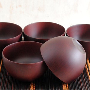May include: Set of five dark brown wooden bowls. The bowls are round and have a smooth, polished finish. They are arranged on a woven bamboo mat.