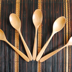May include: Five wooden spoons arranged in a fan shape on a brown bamboo mat.