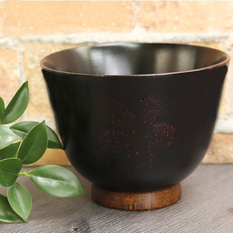 May include: A black wooden bowl with a red floral design. The bowl has a wooden base.
