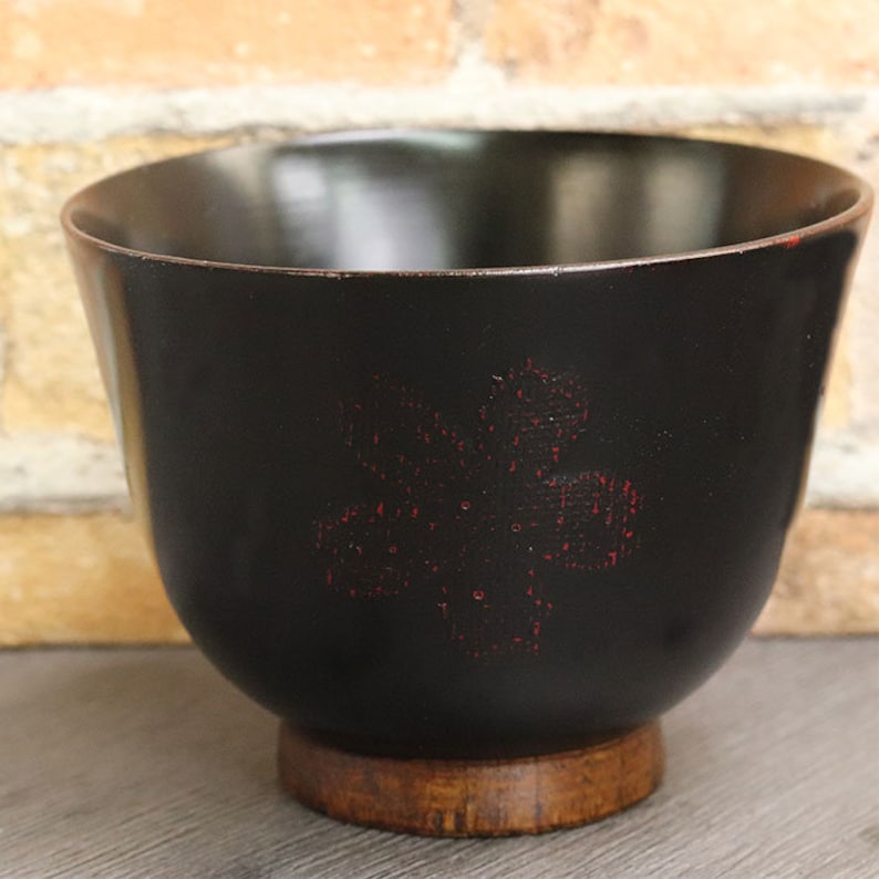May include: A black wooden bowl with a red floral design. The bowl has a wooden base.
