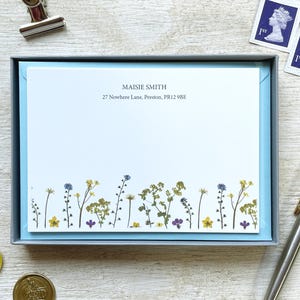 May include: A stationery set with a light blue box holding notecards. The cards display the name "Maisie Smith" and address. The floral design decorates the bottom of the cards. Also includes stamps, a pen, and wax seals.