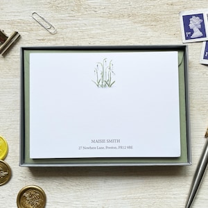 May include: A stationery set with notecards in a grey box. The white notecards have a floral design and the name "Maisie Smith" and address printed on them. Other items include a paper clip, stamps, and wax seals. The address is in Preston.