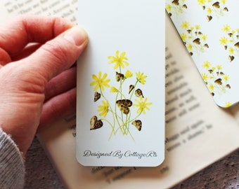 May include: A rectangular white bookmark featuring a botanical illustration of yellow flowers with green stems and dark patterned leaves. The text "Designed By CottageRts" is printed in a black script font at the bottom of the bookmark.