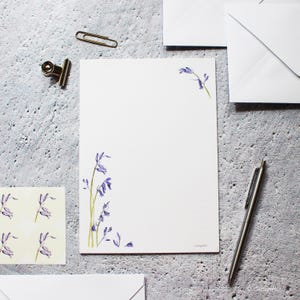 Pode incluir: Um conjunto de papelaria branca com um design floral de campanula azul. A papelaria inclui envelopes e papel para escrever cartas.