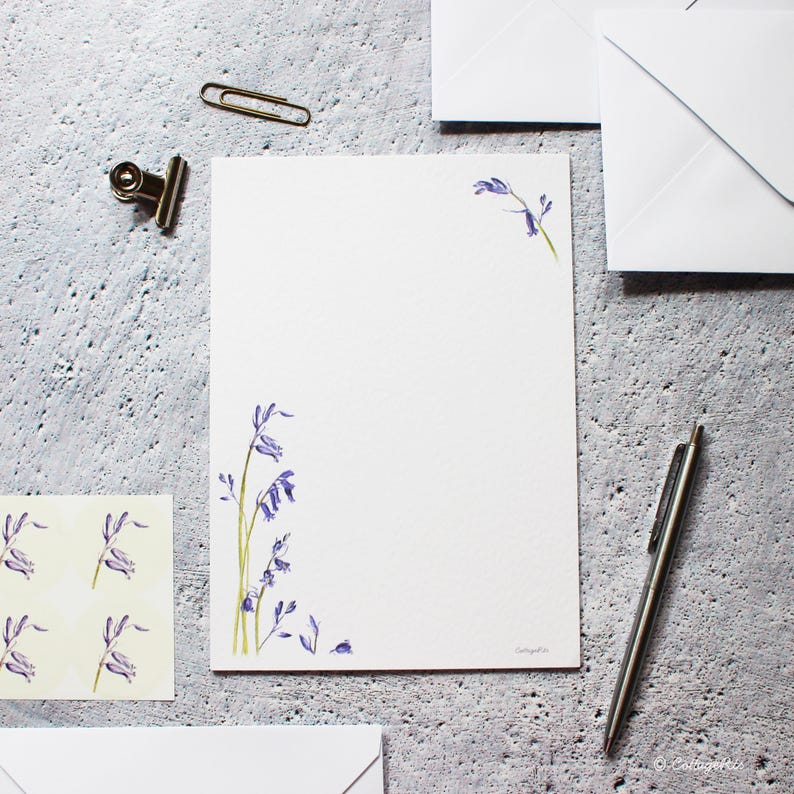 Pode incluir: Um conjunto de papelaria branca com um design floral de campanula azul. A papelaria inclui envelopes e papel para escrever cartas.