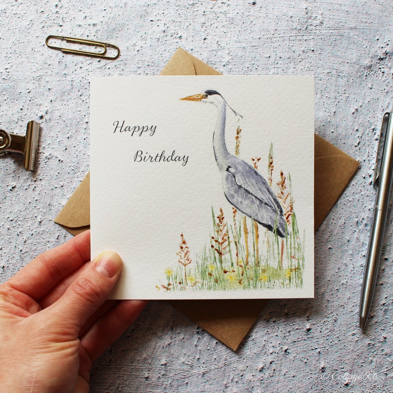 Pode incluir: Um cart&atilde;o branco com as palavras "Happy Birthday" impressas em preto. Uma ilustra&ccedil;&atilde;o em aquarela de uma gar&ccedil;a-azul em p&eacute; em um p&acirc;ntano est&aacute; no lado direito do cart&atilde;o.