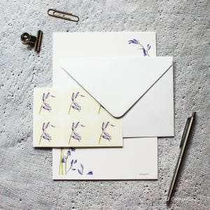 Pode incluir: Um conjunto de papel de carta com campanilhas azuis e um envelope branco. O papel de carta apresenta um fundo amarelo claro com um padr&atilde;o repetitivo de campanilhas azuis. O envelope &eacute; branco liso. O papel de carta tem um desenho de campanilhas azuis no canto inferior.
