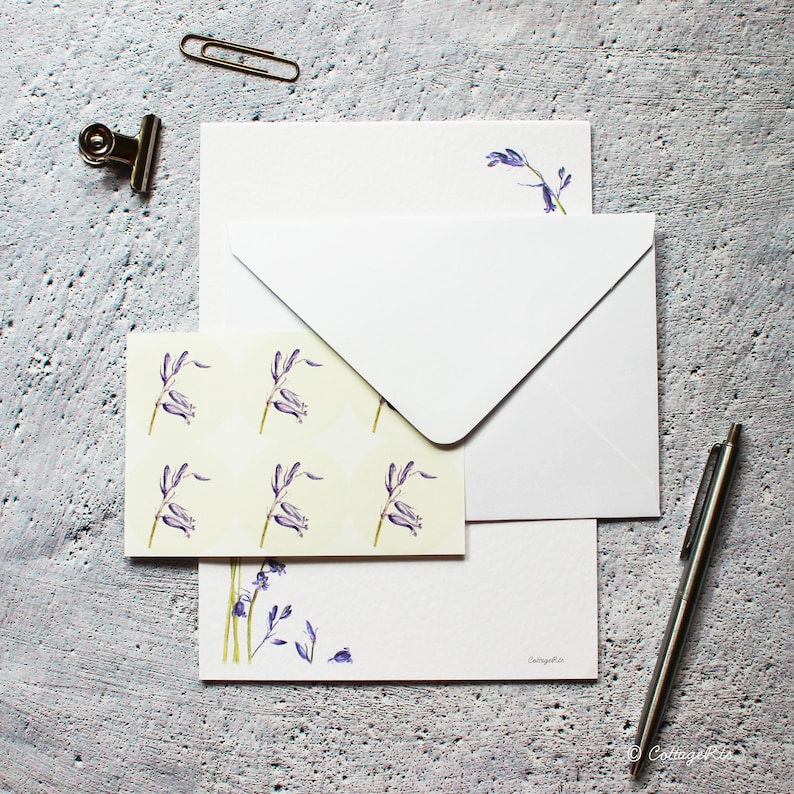 Pode incluir: Um conjunto de papel de carta com campanilhas azuis e um envelope branco. O papel de carta apresenta um fundo amarelo claro com um padr&atilde;o repetitivo de campanilhas azuis. O envelope &eacute; branco liso. O papel de carta tem um desenho de campanilhas azuis no canto inferior.