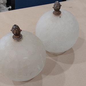 May include: Two white frosted glass globe lampshades with decorative brass finials. The lampshades have a textured surface.