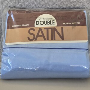 May include: A packaged double satin no-iron sheet set. The packaging features a brown and tan label with the words "Performance Double Satin" and "Our Finest Quality." The sheets are a light blue color.