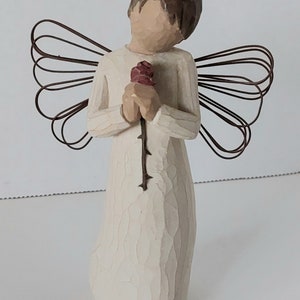 May include: A white wooden angel figurine with brown hair holding a red rose. The angel has wire wings.