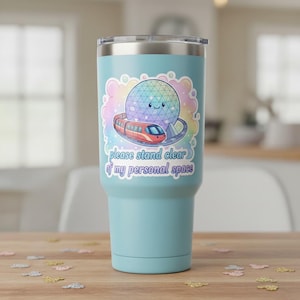 May include: A light blue travel tumbler with a silver lid. The tumbler features a colorful sticker with a smiling geometric sphere, a red train, and the text "please stand clear of my personal space."