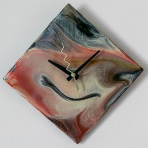 Puede incluir: Un reloj cuadrado con una esfera negra y agujas doradas. La esfera del reloj está hecha de resina y tiene un patrón de remolino de rojo, blanco y negro.