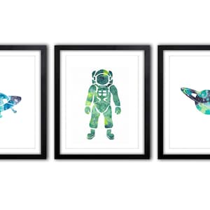 Può includere: Set di tre stampe artistiche incorniciate con illustrazioni ad acquerello a tema spaziale. Le stampe includono un UFO, un astronauta e un pianeta con anelli. Ogni immagine ha uno sfondo bianco ed è incorniciata in una cornice nera.