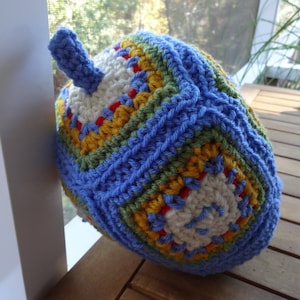 May include: A crocheted hat with a blue, green, yellow, and white color pattern. The hat has a small, pointed top.