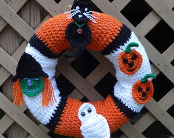 Könnte beinhalten: Ein gehäkelter Halloween-Kranz mit orangefarbenen, schwarzen und weißen Streifen. Er zeigt eine schwarze Katze, eine Hexe, ein Gespenst und zwei Kürbisse.