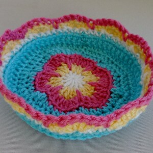 May include: A crocheted bowl with a scalloped edge. The bowl is made in shades of blue, pink, yellow, and white.