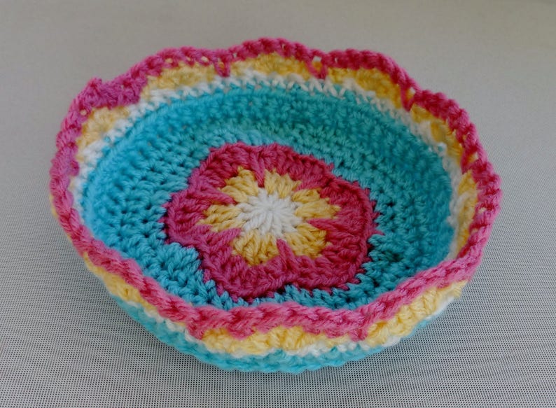 May include: A crocheted bowl with a scalloped edge. The bowl is made in shades of blue, pink, yellow, and white.