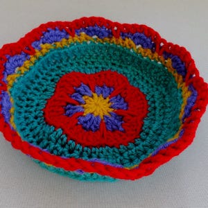 May include: A crocheted bowl with a colorful flower design. The bowl is made with red, yellow, blue, and green yarn.