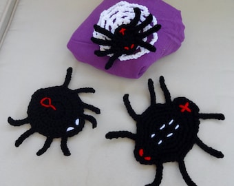 May include: Three black crocheted spiders with red eyes and white details. The spiders are on a white surface.