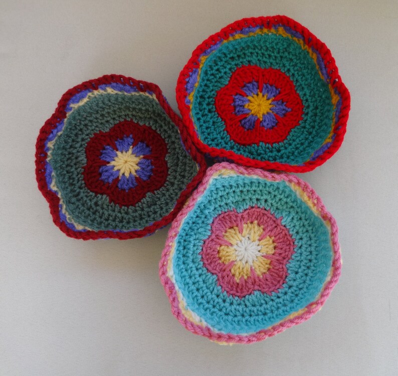May include: Three crocheted bowls with colorful flower designs. The bowls are teal, green, and pink with yellow, red, and white accents.