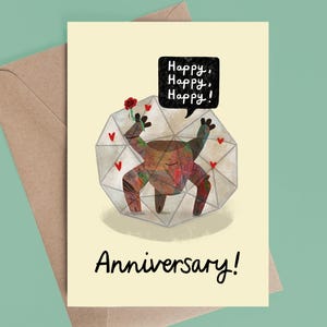 May include: A cream-colored greeting card featuring a brown, multi-legged creature inside a geometric glass shape. The creature holds a red rose, surrounded by small red hearts. A black speech bubble says Happy, Happy, Happy! and Anniversary!