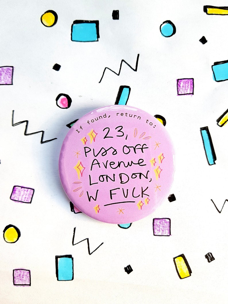 May include: Pink round button with white text that reads "If found, return to: 23, Piss Off Avenue, LONDON, W FUCK". The button is surrounded by a white background with colorful geometric shapes.