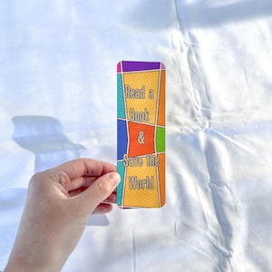 May include: A colorful bookmark with a comic book style design. The bookmark says "Read a Book & Save the World".