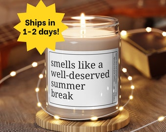 Peut inclure: Une bougie en cire de soja brune avec une étiquette blanche qui indique "smells like a well-deserved summer break". La bougie est posée sur un dessous de verre en bois avec des lumières féériques blanches enroulées autour.