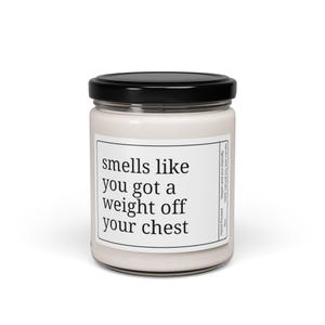 May include: A white candle in a glass jar with a black lid. The label reads "smells like you got a weight off your chest." The candle is hand-poured and made with vegan, eco-friendly, 100% natural soy wax.