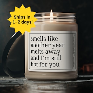 Puede incluir: Un tarro de vidrio con una vela de cera beige en su interior. La etiqueta del tarro dice "smells like another year melts away and I'm still hot for you".