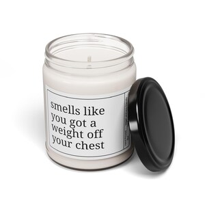 May include: A white scented candle in a clear glass jar with a black lid. The label reads "smells like you got a weight off your chest". The candle is hand-poured and vegan-friendly.