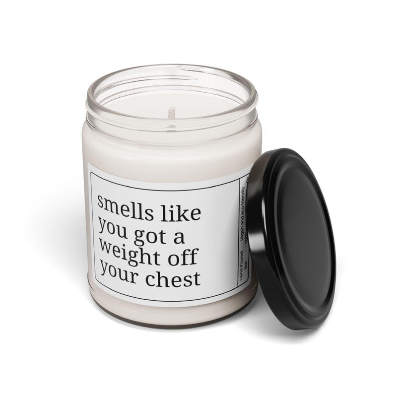 May include: A white scented candle in a clear glass jar with a black lid. The label reads "smells like you got a weight off your chest". The candle is hand-poured and vegan-friendly.