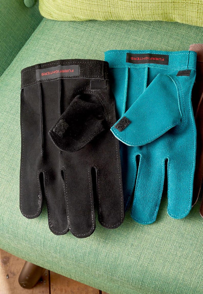 K&ouml;nnte beinhalten: Zwei Paar Wildlederhandschuhe, ein schwarzes und ein blaues Paar, mit dem Text "FURRIGHTER" auf der R&uuml;ckseite jedes Handschuhs.