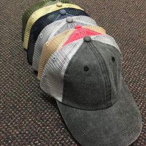 K&ouml;nnte beinhalten: Ein Stapel von sechs Baseballkappen in verschiedenen Farben, darunter Gr&uuml;n, Gelb, Schwarz, Grau, Rot und Dunkelgrau. Die Kappen bestehen aus einem Netzstoff mit einem durchgehenden Frontpanel. Die Kappen sind mit der dunkelgrauen Kappe unten gestapelt.