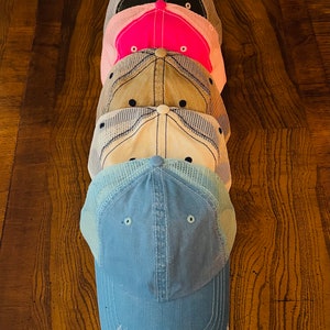 K&ouml;nnte beinhalten: Stapel von f&uuml;nf Baseballkappen in verschiedenen Farben. Die unterste Kappe ist hellblau, die n&auml;chste ist wei&szlig;, die n&auml;chste ist beige, die n&auml;chste ist rosa und die oberste Kappe ist schwarz.